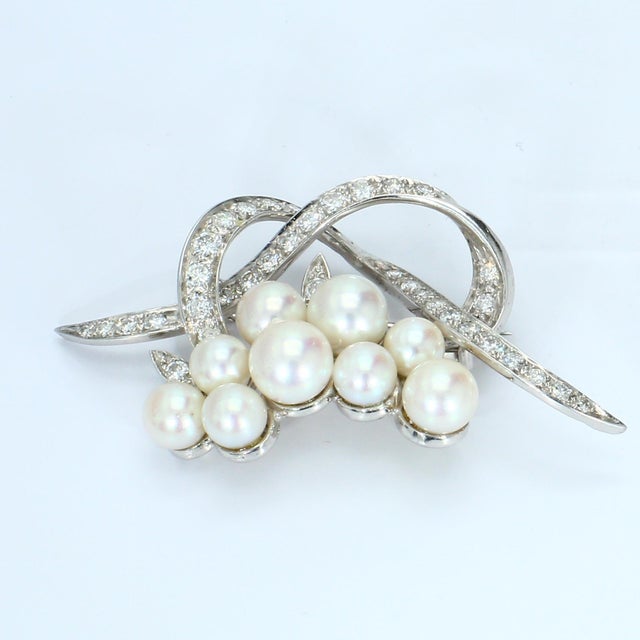 This brooch features a cluster of eight lustrous pearls, elegantly arranged. Curved bands encrusted with white diamonds...