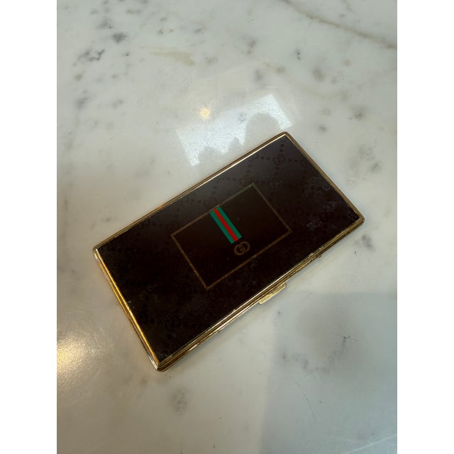 An elegant Gucci cigarette case crafted in Italy during the 1970s, featuring a polished gold-plated frame and a rich dark...