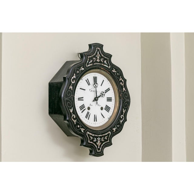 A French Napoleon III wall clock with a lacquered wooden case with inlaid floral decorations surrounding a white enamel...
