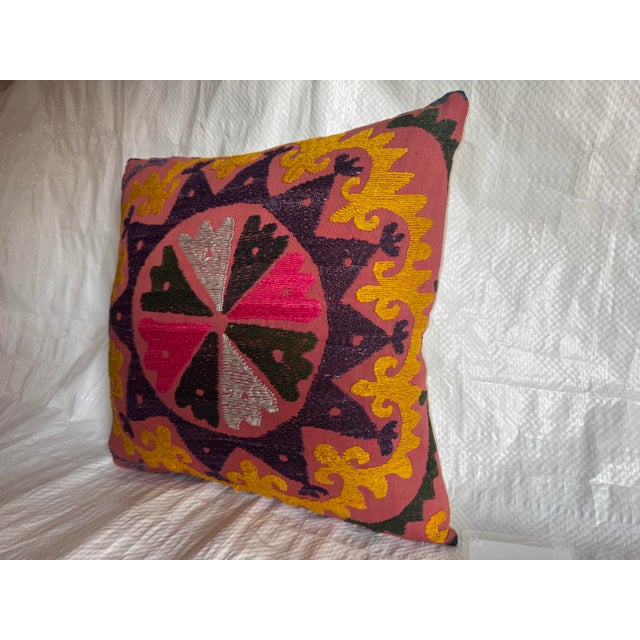 This vivid 1900s Suzani pillow showcases a star-shaped medallion surrounded by swirling motifs in golden yellow, plum,...