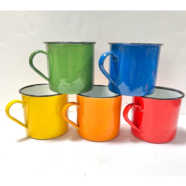 A vibrant set of five 1950s enamelware camp mugs in classic rainbow hues, produced in Hong Kong during the height of mid-...