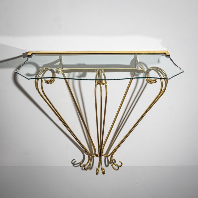 Delicate brass wall console, reflecting the refined elegance of Italian mid-century design. The volute-shaped supports...