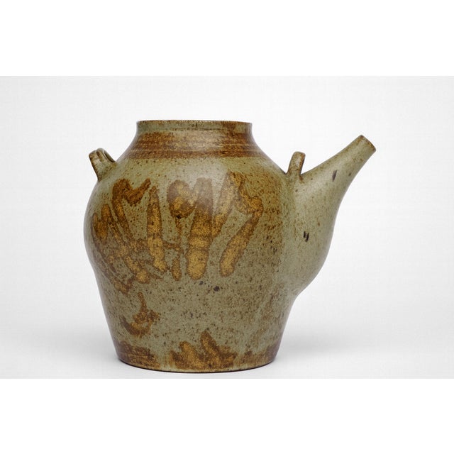 This sculptural pitcher features a broad, rounded body with a sharply angled spout, giving it a strong silhouette for...