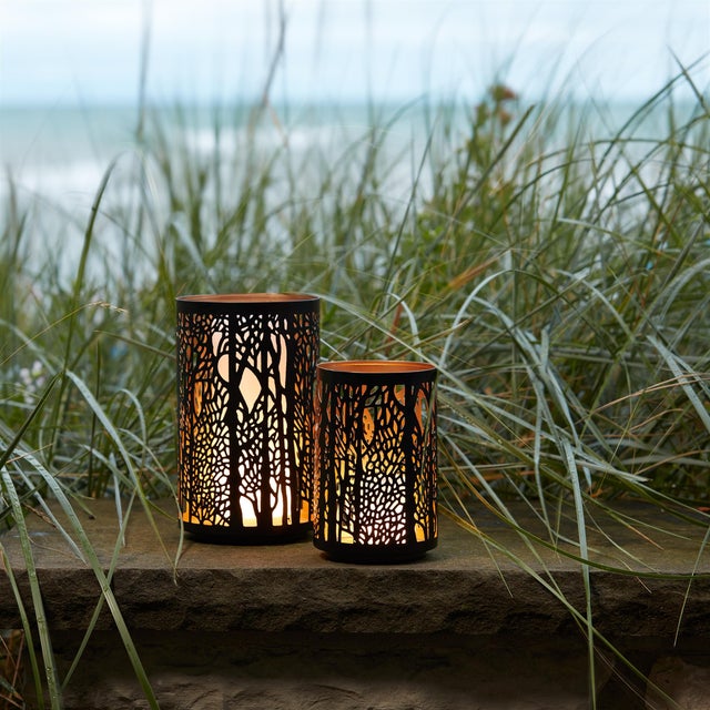 Create a warm, inviting glow in your home with this stunning set of Forest Trees Punched Metal Candle Holders. Designed...