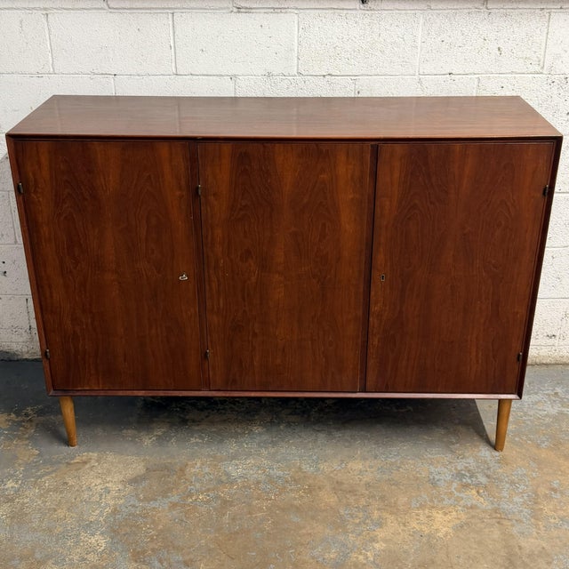 A Danish teak three-door cabinet dating to the 1940s, with a clean rectangular case, raised legs, and simple paneled...