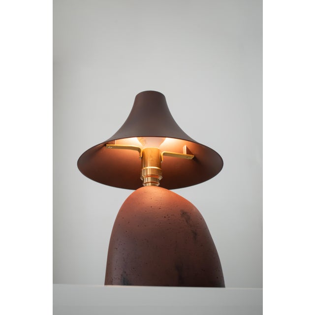 The earth lamp is a handcrafted table lamp in warm, burnt terracotta tones. its solid base, with subtle irregularities and...