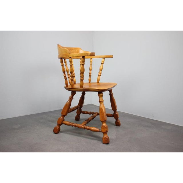 A distinctive vintage Windsor-style armchair dating to approximately the 1970s–1980s, featuring a warm honey-toned wooden...