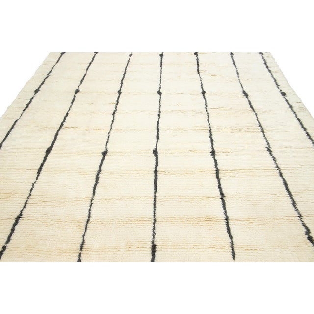 This beautiful contemporary Moroccan-style hand-knotted wool rug has an ivory field and fringes. This plush rug has a...