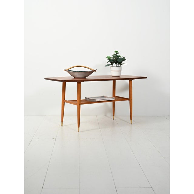 Scandinavian teak coffee table from the 1960s, featuring a boat-shaped top, turned legs with brass tips, and a woven cane...