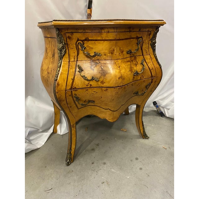 A very stylish diminutive bombe chair or bed side chest. The highly figurative book matched wood with cast brass mounts....