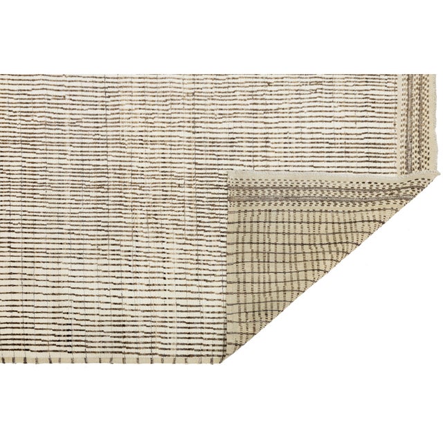 Artisan-crafted modern Moroccan wool rug featuring irregular vertical stripes in black on a warm ivory ground. The...