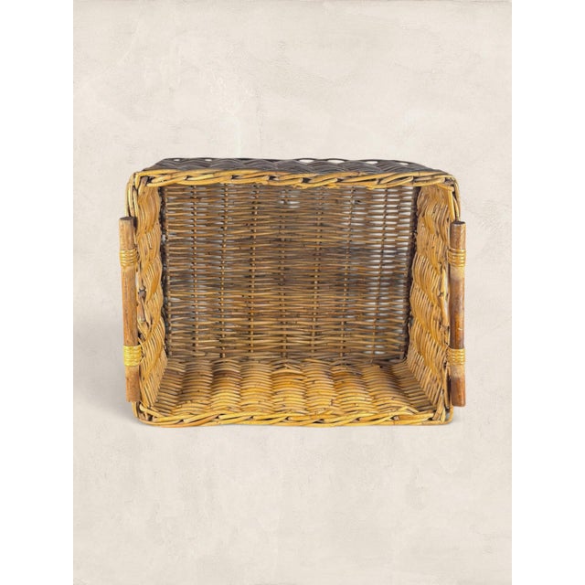 A charming English wicker storage basket featuring a handwoven rectangular form and turned wooden handles. Its warm honey-...