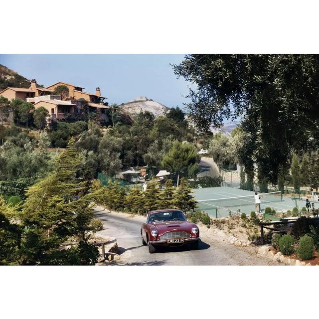 Il Pellicano Tennis 1973 An Aston Martin DB6 sports car driving past the tennis courts at Il Pellicano Hotel in Porto...
