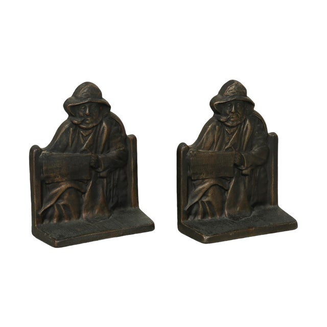 A pair of cast iron Cape Cod fisherman bookends. The fisherman smokes a pipe and is reading the newspaper ‘the I&M’....