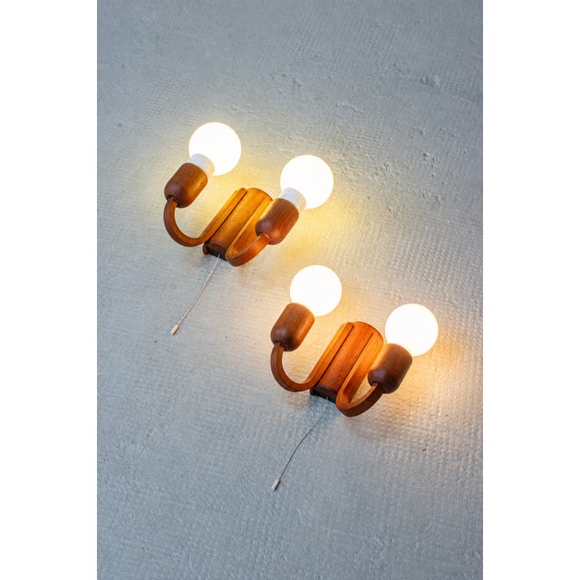 These two wall lights from Domus combine warm teak wood with a particularly beautiful, symmetrical design. Two softly...