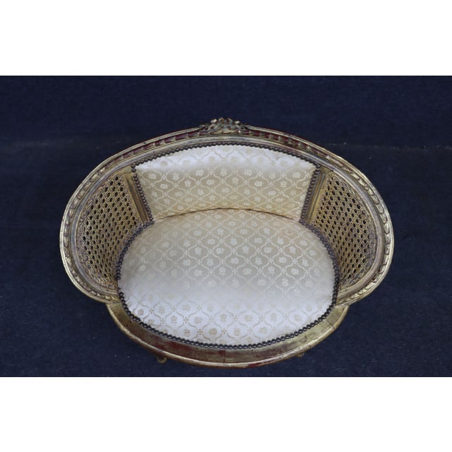French Louis XVI style barrel chair featuring a carved giltwood frame with hand-caned sides and back, a carved floral...