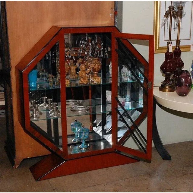 Octagonal cherry vitrine with ebonized wood. Mirrored interior, three glass shelves and center door. Mounted on a...