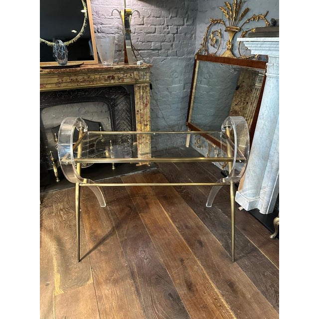 An elaborately designed acrylic and lacquered brass console table. The X frame supports a mix of brass and scrolled...