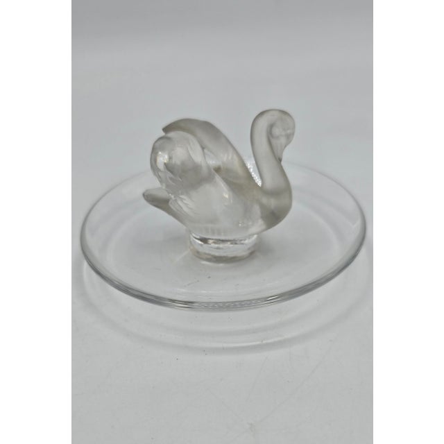Lalique ring holder in molded pressed white crystal with a satin and polished finish, depicting a swan on a circular base....