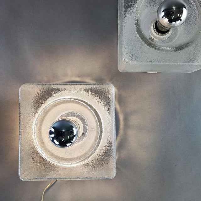 A pair of cubic murano glass wall lamps. They create a warm light that contrasts with the frosted glass. They include an...