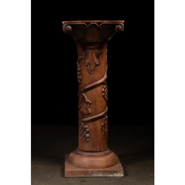 Decorative carved wooden pedestal featuring a substantial cylindrical shaft enveloped by high-relief grapevine...