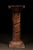 Decorative carved wooden pedestal featuring a substantial cylindrical shaft enveloped by high-relief grapevine...