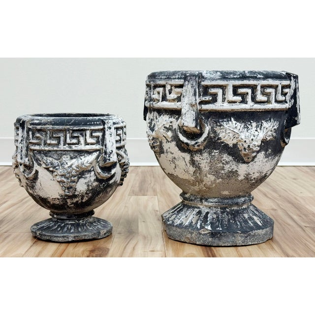 Vintage pair of white washed concrete planters. Urn shape with a Greek key pattern to top of each planter and grape design...