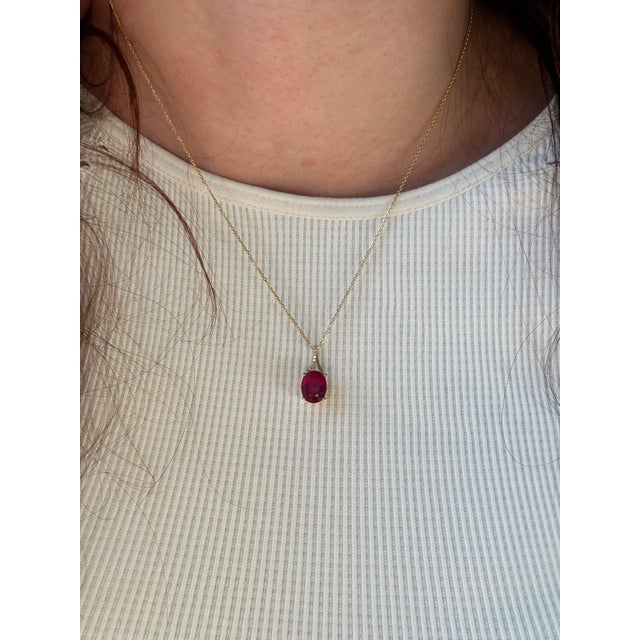 A Madagascar ruby glows with red brilliance at the heart of this oval pendant, framed by a trail of brilliant natural...
