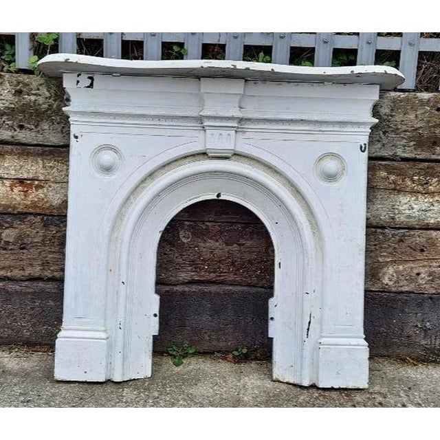 A substantial antique Victorian cast iron fireplace, distinguished by its elegant arched opening, broad architectural...