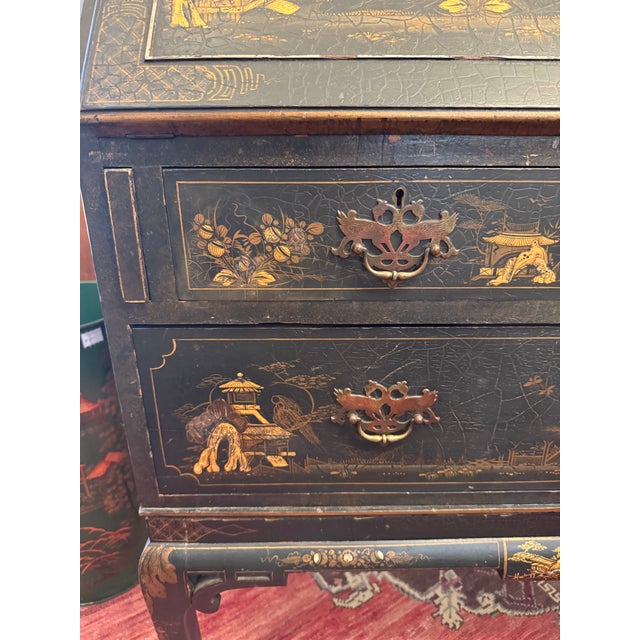 Drop front black chinoiserie desk. Gilded chinoiserie figures. 3 bottom drawers, 3 small desk drawers and cubbies behind...