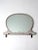 An antique oval mirror featuring a decorative wooden frame with a lipped base and original crackled white paint. The aged...