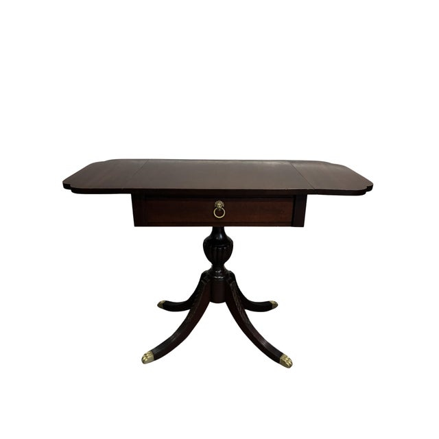 An elegant antique English Regency style mahogany drop-leaf side table featuring a rectangular top with two folding...