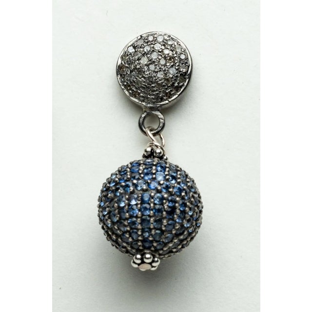 A pair of ball drop earrings with round, faceted blue sapphires in a pave` setting covering the entire ball. The post is...