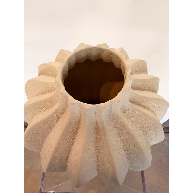 Contemporary sculptural vase featuring a soft ivory finish and a distinctive fluted silhouette with organic, carved...