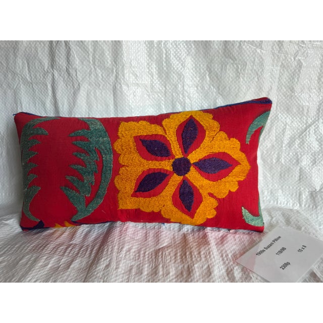 A vivid early 20th-century Suzani pillow embroidered with bold floral motifs in shades of golden yellow, plum, and green...