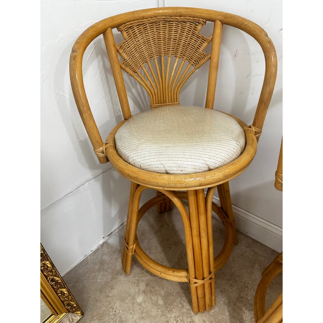 A set of Three Vintage Coastal Style Wicker Rattan Swivel Bar Stools. circa 1980s Feature a Rattan frame, cane detailing...