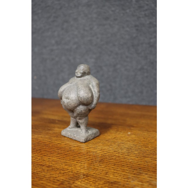 Antique hand-carved stone figure depicting a stout, pot-bellied man standing with his hands behind his back on a...