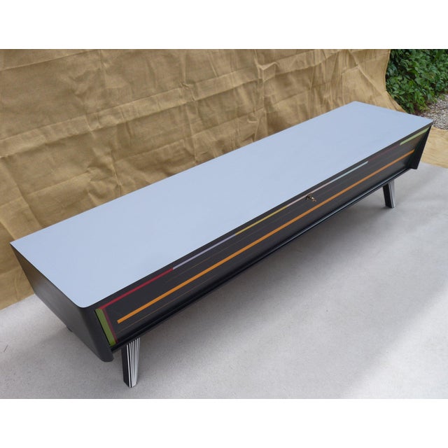 Vintage low sideboard with one drop-down door opening to reveal two drawers and two pull-out shelves. "Mist" laminate top...
