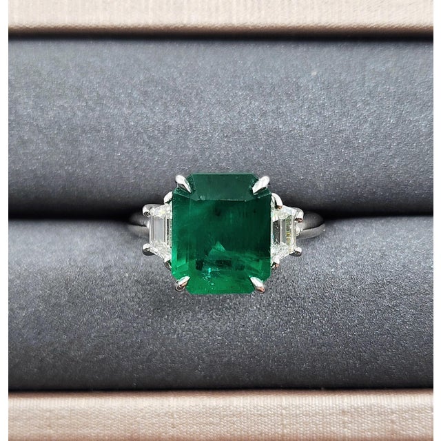 This striking cocktail ring showcases a captivating design centered around a vibrant GIA-certified emerald-cut emerald....