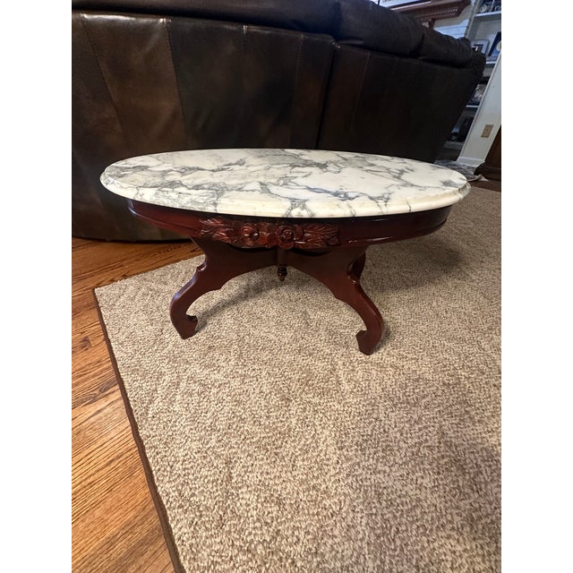 Elegant vintage oval marble-top coffee table featuring a beautifully carved floral and leaf apron, classic cabriole legs,...