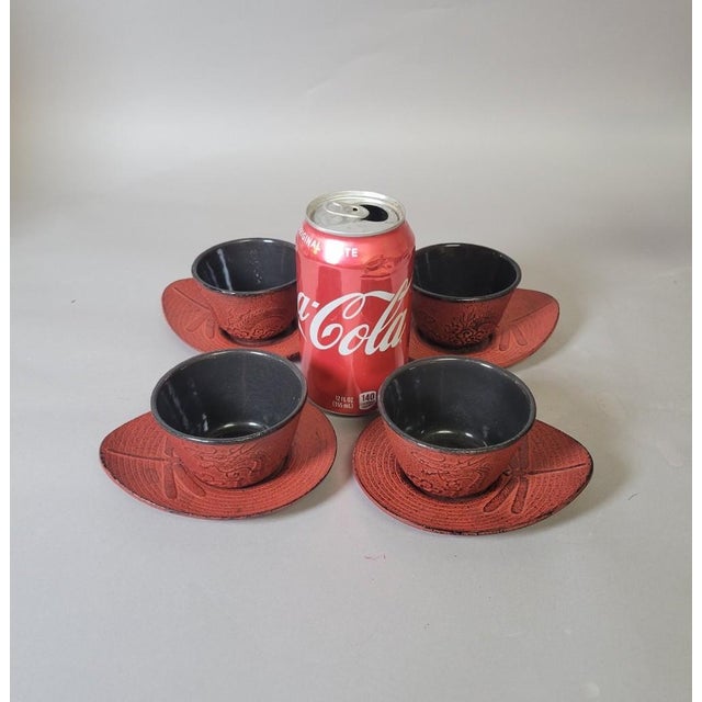 Vintage Japanese cast iron tea cup and saucer set featuring four red-orange cups with black porcelain-enamel interiors,...