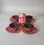 Vintage Japanese cast iron tea cup and saucer set featuring four red-orange cups with black porcelain-enamel interiors,...