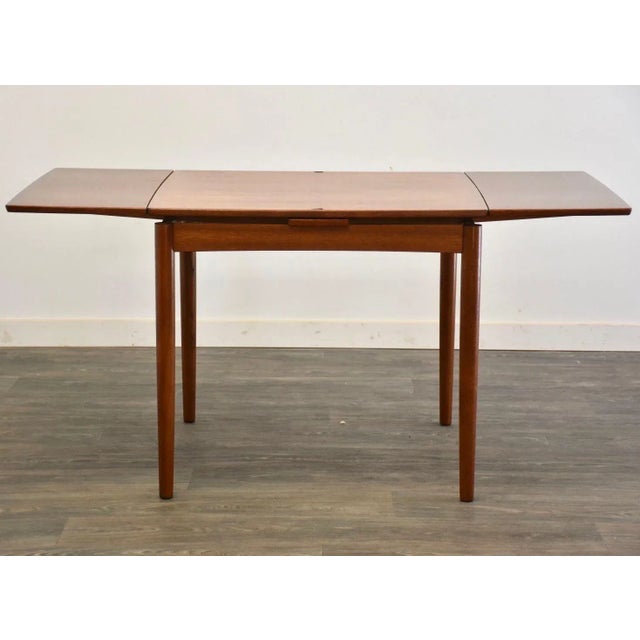 A mid century modern teak draw leaf dining table fully extends to 56.5”. Reversible black vinyl top. Shows some...