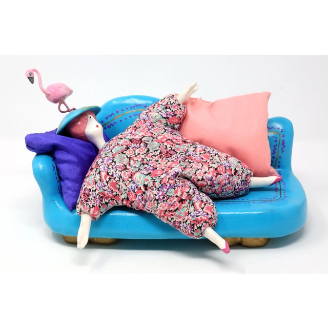 A unique, vintage 1995 handmade art piece, composed of a ceramic blue sofa, two pillows, and a doll with porcelain hat...