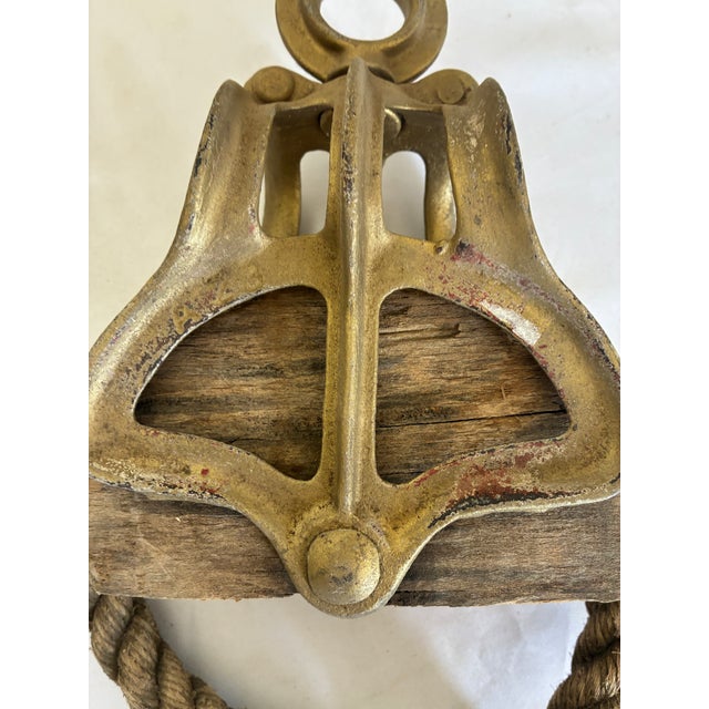 A substantial vintage nautical pulley block featuring a solid wood body encased in a heavy cast metal frame, complete with...