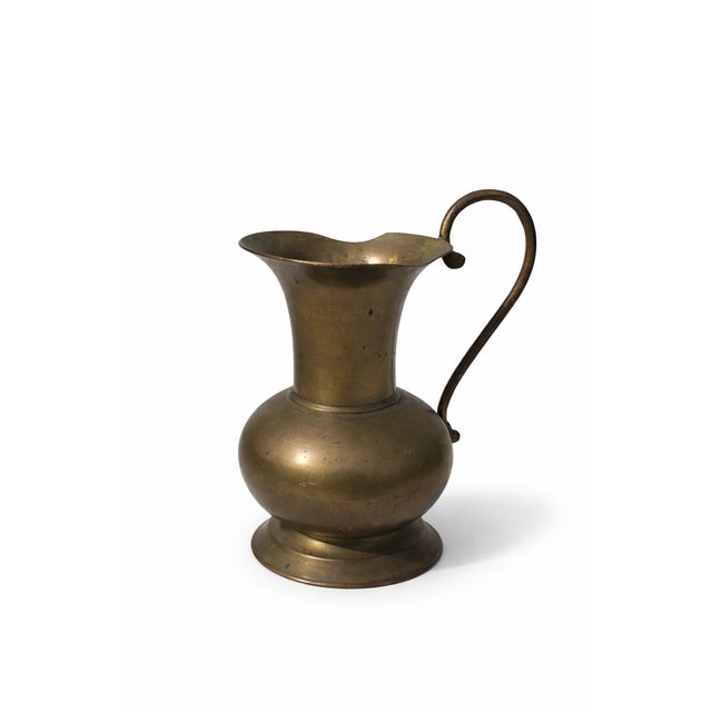 A beautifully aged vintage brass pitcher featuring a classic rounded body, gracefully curved handle, and gently flared...