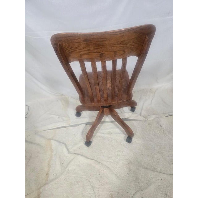 Handsome vintage oak swivel desk chair featuring a classic banker's chair silhouette with a contoured wood seat, six-...