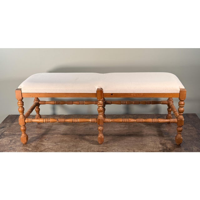 This vintage French country style wooden upholstered bench features a long rectangular seat in neutral linen fabric over a...