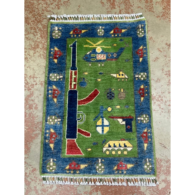 Afghan war rug, hand-knotted in Afghanistan from 100% wool. Measuring 2’ x 2’11”, the rug features a distinctive pictorial...