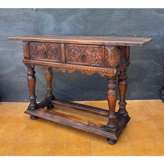 Spanish Renaissance Revival console crafted in solid oak, featuring two deeply carved drawers and a structural lower...